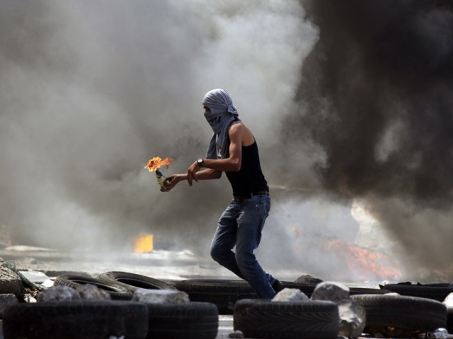 Palestinian throws a Molotov cocktail at Qalandiya refugee camp, August 26, 2013